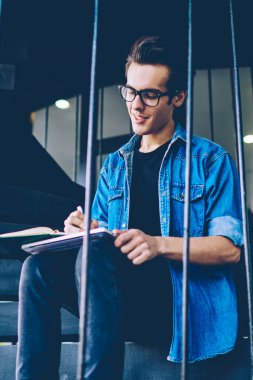 Bir sonraki mülakat için ana soruları yazan pozitif erkek gazeteci, kampüs merdivenlerinde ders kitabı ile otururken, başarılı hipster adam üniversite sınavına hazırlanıyor ve öğrenme için bilgi notları