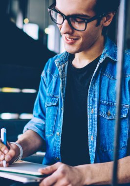 Gülen erkek öğrenci tasarımcı açık merdivenlerde serbest zaman sırasında eğitim için ders kitabında çizim skeçler, gözlük olumlu hipster adam boş defteriyi fikir ile kompozisyon yazma