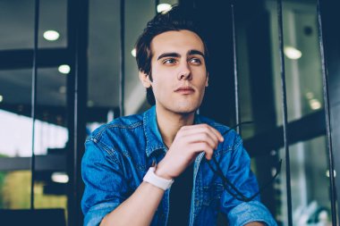 Kampüs merdivenlerinde otururken gözlük tutan ve iletişim için arkadaş bekleyen ciddi erkek öğrenci, kot pantolon t shirt trendy hipster adam boş zamanlarında gelecekteki yaşam hakkında düşünme düşünme