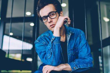 Optik gözlük yakışıklı ciddi hipster adam kentsel oturma oturan ve hayat hakkında düşünürken arkadaşı dışarıda beklerken, kot giyim genç kafkas adam kampüste düşünme hissi