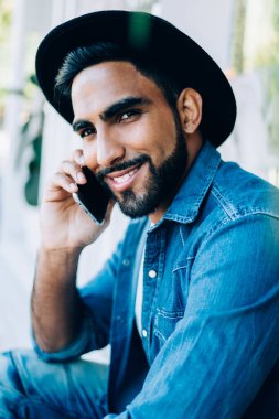 Şık giyinmiş yakışıklı hippinin yakın plan portresi. Kameraya bakıyor. Cep telefonu uygulaması üzerinden uluslararası bir konuşma yapıyor.