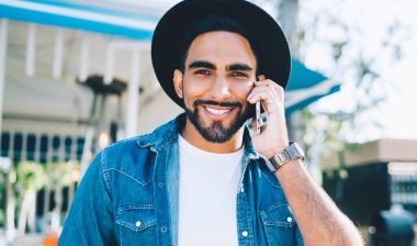 Cep telefonu görüşmeleri sırasında arkadaşlarıyla görüşürken gülümseyen neşeli İspanyol hipsterin yarım boy portresi. Akıllı telefondan arayan başarılı bir adam.