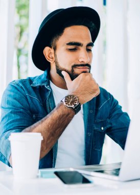 Şık şapkalı düşünceli genç adam internet sitesinden ilginç webinar izliyor sokak kafeteryasında iyi internet bağlantısı olan programcılar için, hipster adam video çağrısı alıyor.