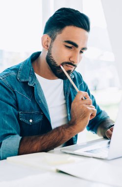 Düşünceli hippi, üniversitenin internet sitesinden bilgisayardan gelen bilgileri inceliyor. İnternete dosya indirmek için 4G 'ye bağlanan düşünceli bir adam.