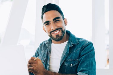 Yüzünde sevimli bir gülümseme olan neşeli bir hippi portresi açık dizüstü bilgisayarla internetteki işine ara veren İspanyol erkek serbest çalışan iyi bir internet bağlantısı olan sokak kafeteryasında oturuyor.