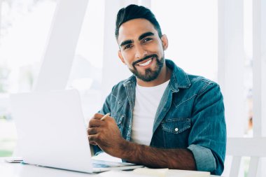 Yüzünde sevimli bir gülümseme olan neşeli bir hippi portresi açık dizüstü bilgisayarla internetteki işine ara veren İspanyol erkek serbest çalışan iyi bir internet bağlantısı olan sokak kafeteryasında oturuyor.