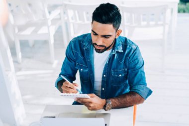 Çevrimiçi internet sitelerindeki ucuz biletleri araştırmak için dizüstü bilgisayarla kafeteryada oturan organizasyon yazarları hakkında bilgi içeren bir ders kitabı tutan deneyimli genç turist.