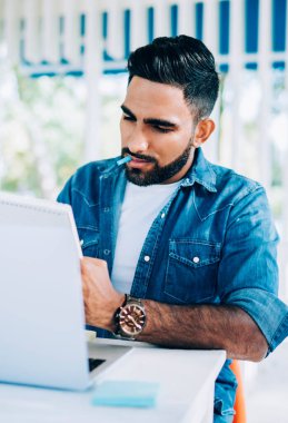 Şık giyinen İspanyol hippi, uzak çalışma ile büyülenmiş ders kitabında proje fikirleri yazıyor, kafeteryada iyi internetli kitaplar yazıyor ve not defterine notlar yazıyor.