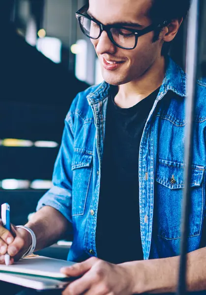Gülen erkek öğrenci tasarımcı açık merdivenlerde serbest zaman sırasında eğitim için ders kitabında çizim skeçler, gözlük olumlu hipster adam boş defteriyi fikir ile kompozisyon yazma