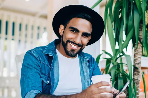 Havalı kıyafetler giymiş mutlu bir adamın portresi. Elinde yemek kupası ve akıllı telefon aleti ile dışarıda oturuyor. Boş zamanlarında kameraya gülümsüyor.