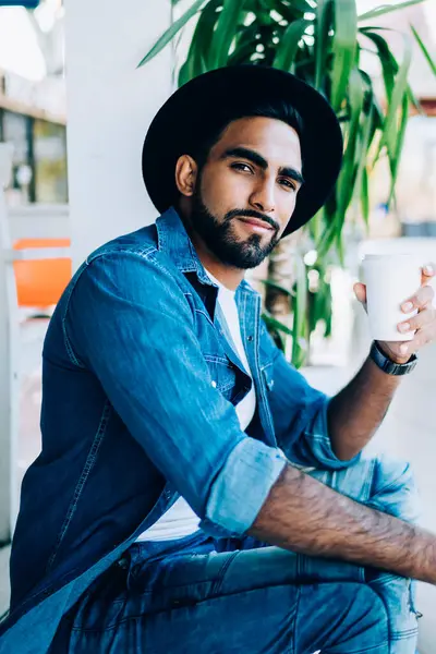Elinde cep telefonu olan, elinde kağıt bardakla lezzetli kafeinli kahve bardağı tutan ve kameraya bakan yakışıklı sakallı adamın portresi.