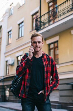 Moda kıyafetleri içinde, el ele tutuşup kameraya bakarken şehrin caddesinde duran ve akıllı telefondan konuşan olumlu bir adam.