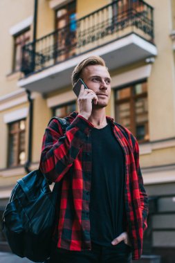 Sırt çantalı yakışıklı bir adam. Elini cebine atıp, gözlerini kaçırıyor. Şehir caddesinde dikilip, akıllı telefon konuşmaları yapıyor.