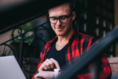 Modern dizüstü bilgisayarı olan yakışıklı, gülümseyen ve bildirim ile akıllı bir adama bakan şehir caddesindeki evlerin önünde serbest iş yapan.