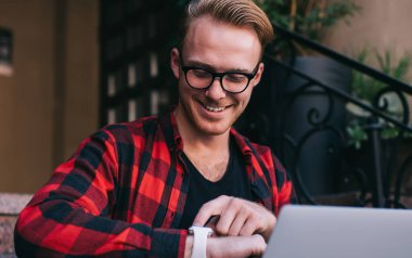 Şık gözlüklü ve kareli tişörtlü yakışıklı. Neşeli bir şekilde gülümseyen ve akıllı adam. Evin dışındaki merdivenlerde modern dizüstü bilgisayar kullanıyor.