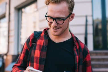 Yakışıklı adam şık kıyafetler içinde gülümsüyor ve şehir caddesinde yürürken modern akıllı telefonlara bakıyor ve sıcak içeceklerin tadını çıkarıyor.