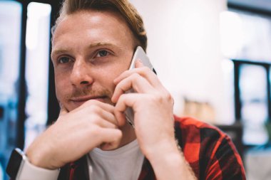 Kareli gömlekli yakışıklı, çenesini ovuşturup, rahat bir kafenin bulanık arka planında akıllı telefon konuşması yaparken düşünüyor.