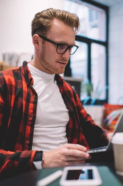 Moda gözlüklü yakışıklı bir adam ve modern dizüstü bilgisayarda gezinirken şık bir kafede masa başında serbest çalışıyor.