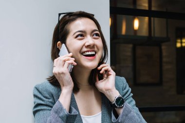 Kot pantolon ve modaya uygun ceketli çekici Asyalı kadın kafasının üstünde güneş gözlüğü ile kafenin duvarına yaslanıyor ve telefon görüşmeleri sırasında gözlerini kaçırıyor.