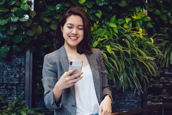 Mutlu, genç, gülümseyen, şık kıyafetler içinde güzel bir Asyalı kadın. Telefondaki mesajları kontrol ediyor. Gri ceketli ve kot pantolonlu.