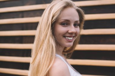 Şen şakrak beyaz modelin yakın portresi. Yüzünde sevimli bir gülümseme var. Kameraya bakıyor ve şehir ortamında boş zamanlarında gülüyor.