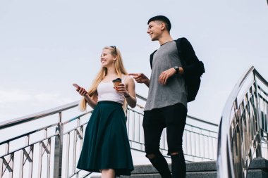 Gündüz vakti merdivenlerden cep telefonu ve dondurmayla inen sıradan giyinen genç adam ve kadının alçak açısı.