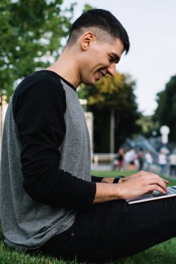 Neşeli erkek metin yazarının açık havada açık havaya bağlanan metin uygulamalarında fikirler yazması, mutlu gülümseyen öğrenci ve web sitesindeki bilgileri kullanarak öğrenmesi yan görünümü