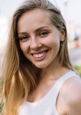 Kameraya gülümseyen ve açık havada eğlenen neşeli beyaz dişli neşeli hippi kız portresi. Şehir ortamında gülen sarı saçlı mutlu beyaz kadın.