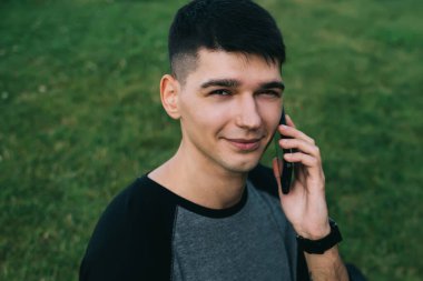 Parkta dizüstü bilgisayarla çalışırken ve sınava hazırlanırken cep telefonuyla konuşan ve kameraya bakan sıradan bir kız öğrenci.