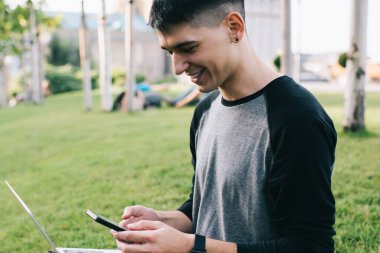 Şehir parkındaki iş sırasında akıllı telefon ve dizüstü bilgisayarla medya dosyalarını paylaşan yakışıklı hippi, cep telefonundaki mesajları uzaktan kontrol eden pozitif erkek serbest yazar.