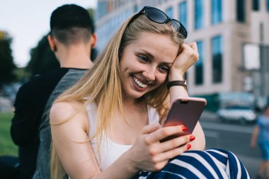 Cep telefonu cihazıyla samimi hippi kız internet sitesinde komik içerik yayınları okuyor. Modern akıllı telefon ve 4G kablosuz internet kullanıyor. Cep telefonlu mutlu kadın alışverişi yapıyor.