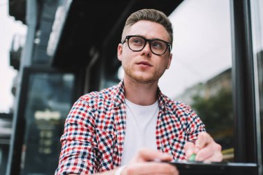 Günlük giysiler ve gözlüklerle konsantre olmuş serbest çalışanların bakış açısıyla başlangıç notları üzerinde çalışırken sokak kafesindeki masada otururken başka yöne bakıyor.