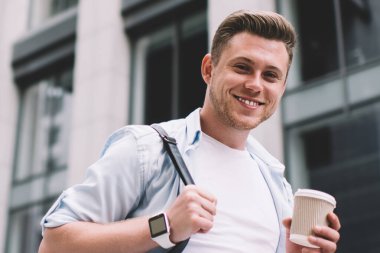 Sırt çantalı yakışıklı bir adamın kameraya gülümserken bir fincan kahve içmesinden.