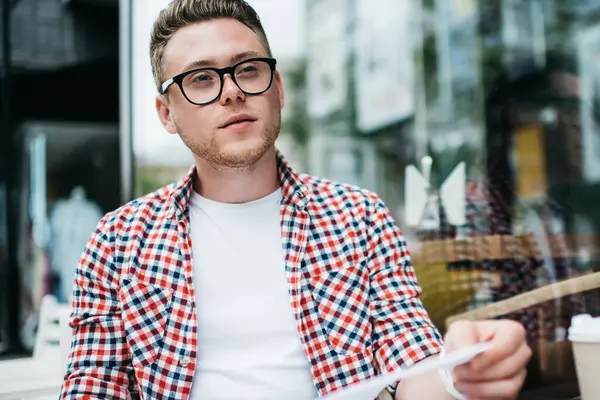 Günlük giysiler ve gözlüklerle serbest çalışan, proje üzerinde çalışan sokak kafeteryasında oturan ve gözlerini kaçıran biri.