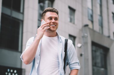 Düşük açılı, güler yüzlü stil sahibi bir erkek. Sokakta merdivenlerde dikilip gözlerini kaçırırken cep telefonuyla konuşuyor.