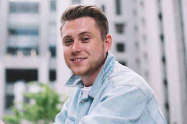 Modern şehrin sokaklarında camdan çitlere yaslanmış, sıradan giyinmiş, neşeli, yakışıklı bir erkek. Kameraya bakıyor.