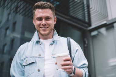 Alttan gülümseyen, şık kot ceketli, sırt çantalı, elinde kahve fincanı olan beyaz bir adam kameraya bakıyordu.