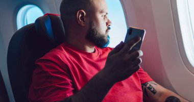 El ele tutuşan genç adam koltukta kendini rahat hissediyor. Düşünceli erkek uçuş yolcusu kabin penceresinin yanında otururken kablosuz bağlantı kuruyor. Uçak çevrimdışı kip