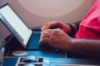 Uçaktaki kablosuz internete dokunmatik ped ile bağlanan genç bir uçuş yolcusu uçak kabin penceresinin yanında oturuyor. Ağ şablonu için boş ekranı, serbest çalışma için dijital göçebe işini düzenle