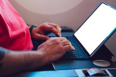 Uçaktaki kablosuz internete dokunmatik ped ile bağlanan genç bir uçuş yolcusu uçak kabin penceresinin yanında oturuyor. Ağ şablonu için boş ekranı, serbest çalışma için dijital göçebe işini düzenle