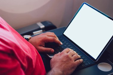 Uçaktaki kablosuz internete dokunmatik ped ile bağlanan genç bir uçuş yolcusu uçak kabin penceresinin yanında oturuyor. Ağ şablonu için boş ekranı, serbest çalışma için dijital göçebe işini düzenle