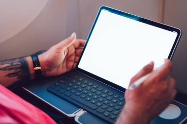 Uçaktaki kablosuz internete dokunmatik ped ile bağlanan genç bir uçuş yolcusu uçak kabin penceresinin yanında oturuyor. Ağ şablonu için boş ekranı düzenle, kalem ile tablete dokun