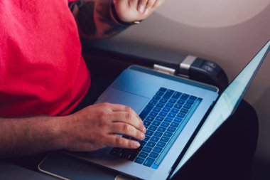 Uçaktaki kabin penceresinin yanında otururken dizüstü bilgisayarla kablosuz internete bağlanan genç adam uçuş yolcusu. Dizüstü bilgisayarda metin yazılıyor, dijital göçebe serbest çalışıyor