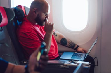 Uçak kabin camının yanında rahat bir uçak koltuğunda otururken uçakta film izleyen genç adam. Beyaz adam birinci sınıf seyahatin tadını çıkarıyor.