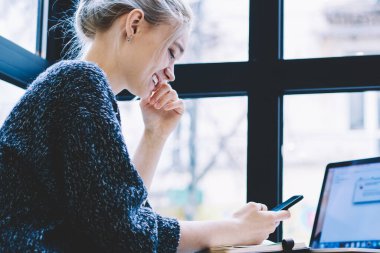 Cep telefonu ile ağ tarama yaparken akıllı telefonda komik video içeriği izlerken mutlu gülmek kadın. Kahve dükkanında otururken hücresel internette gülümseyen milenyal teknoloji Kullanıcı sörf