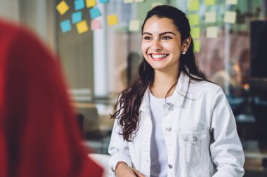 Güzel, genç, gelişigüzel esmer kız beyaz tahtanın yanında duruyor ve yeni bir proje yaratmak için toplanan öğrencilerle mutlu bir şekilde sohbet ediyor.