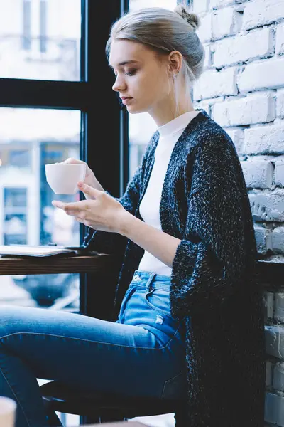 Pencere sokak görünümü ile kahve dükkanı iç rekreasyon süresi harcama sırasında küçük sarışın kadın rahatlatıcı ve kapuçino ısınma fincan zevk yan görünümü