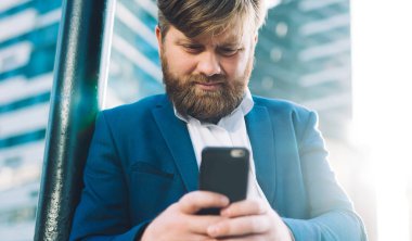 Ciddi profesyonel değişim uzmanı cep telefonu ve metin stratejisi ile şehir merkezinde duruyor, cep telefonu cihazıyla beyaz adam dışarıda iş ortağı bekliyor SMS 'leri kontrol ediyor.