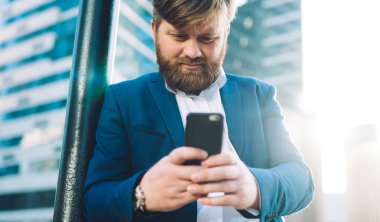 Ciddi profesyonel değişim uzmanı cep telefonu ve metin stratejisi ile şehir merkezinde duruyor, cep telefonu cihazıyla beyaz adam dışarıda iş ortağı bekliyor SMS 'leri kontrol ediyor.