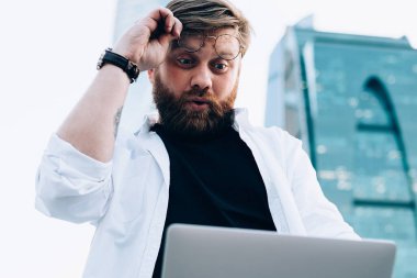 Heyecanlı erkek blogcu dışarıda içerik metni okurken dizüstü bilgisayar istatistiklerinden gelen şaşkınlığa uğramış, internetteki web sitesini izleyen hipster hayranı adam Netbook 'taki içerikten hayrete düşmüş.
